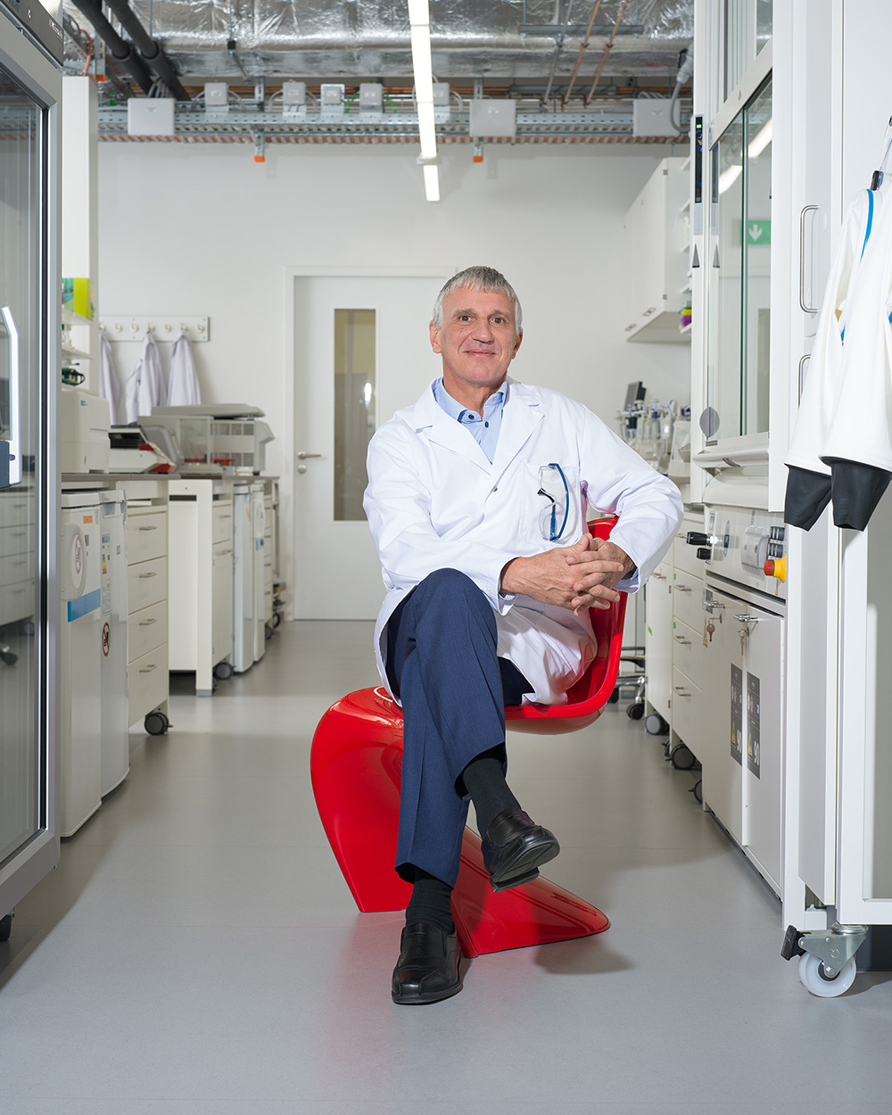 Mann in Laborkittel sitzt in Labor auf rotem Panton Chair