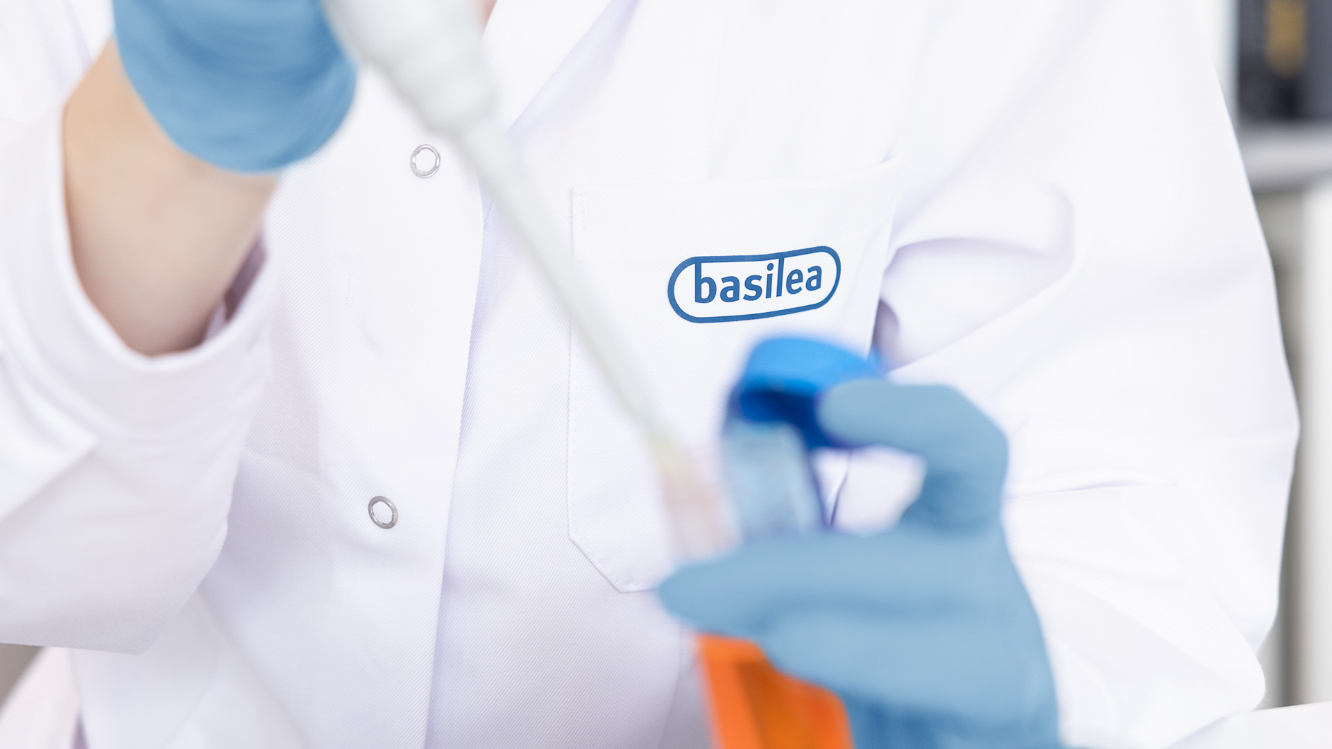 Close Up pipettierende Forscherin mit Basilea Logo auf weissem Laborkittel